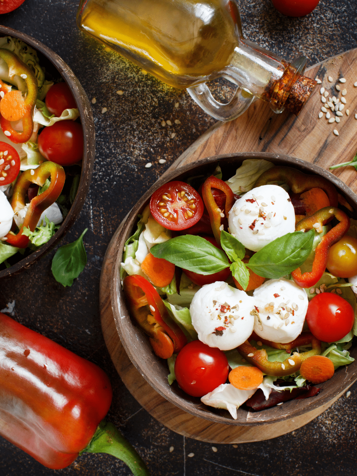 Two bowls of salad with mozzarella and tomatoes in a wooden bowl.