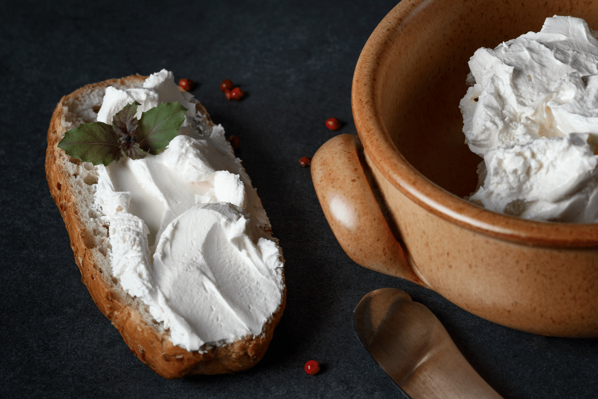 A bowl of cream cheese, a substitute for burrata cheese, next to a loaf of bread.