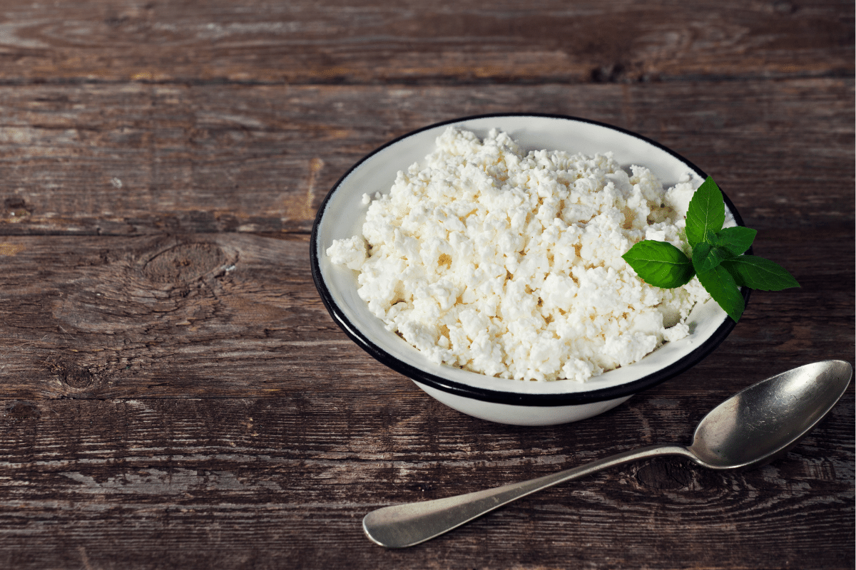 Cottage Cheese in a bowl with a spoon on a wooden table.