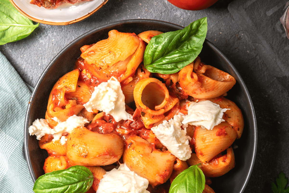A bowl of pasta with tomato sauce, basil and ricotta cheese.