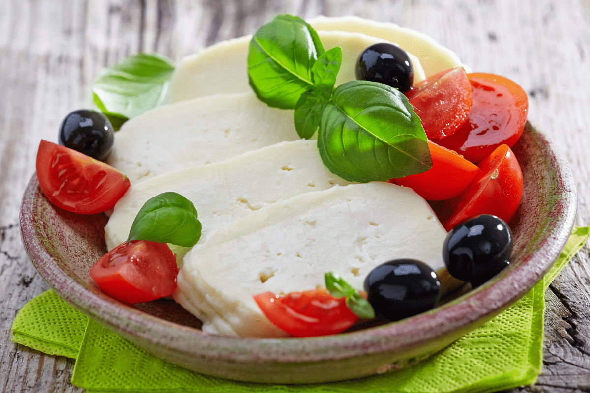 A bowl of feta cheese with tomatoes, olives and basil.