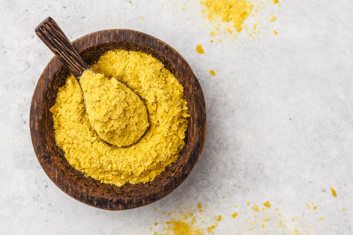 Nutritional Yeast in a wooden bowl with wooden spoon in it.