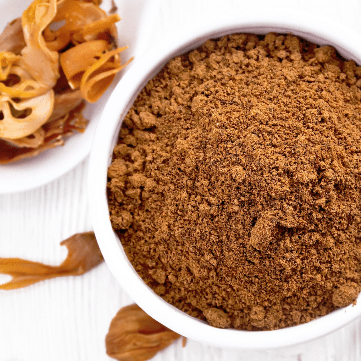 Cinnamon powder, a substitute for mace, in a bowl on a white table.