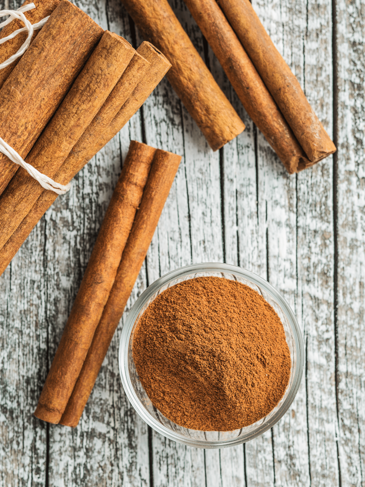 Cinnamon sticks and cinnamon powder in a small glass bowl on a wooden table.