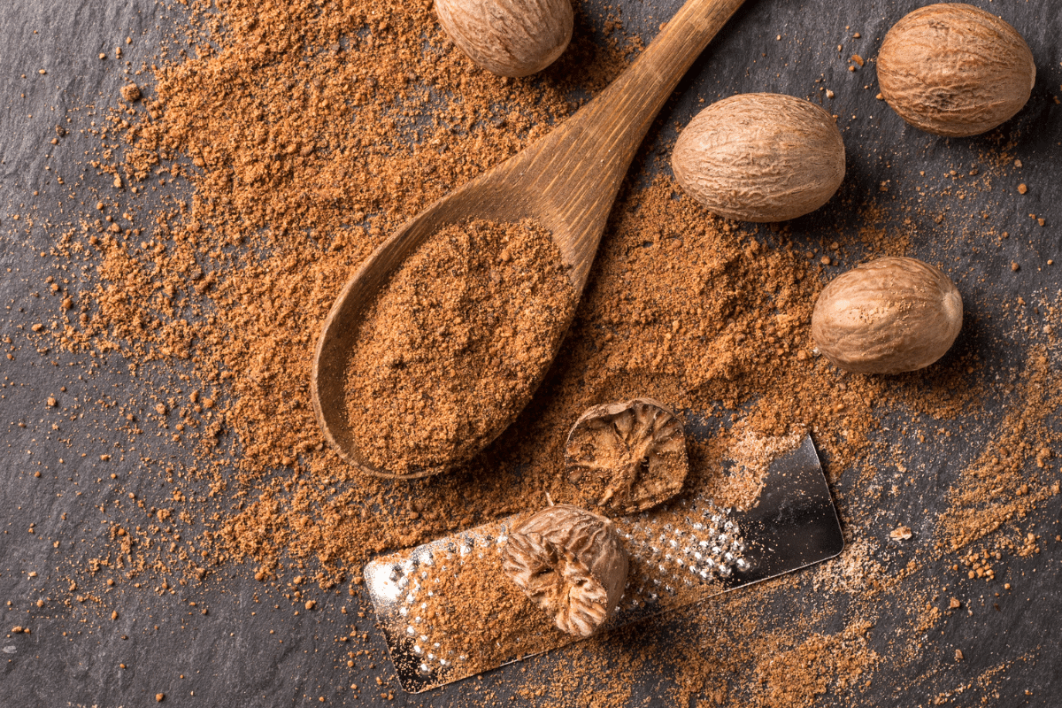 Nutmeg powder, cinnamon substitute on a dark background with wooden spoon and grater.