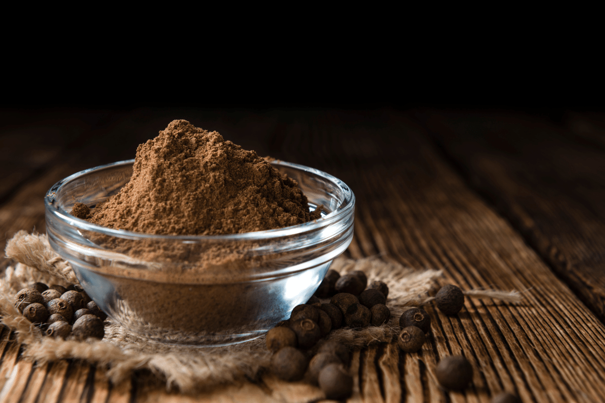 Allspice powder, a cinnamon substitute, in a glass bowl on a wooden table.