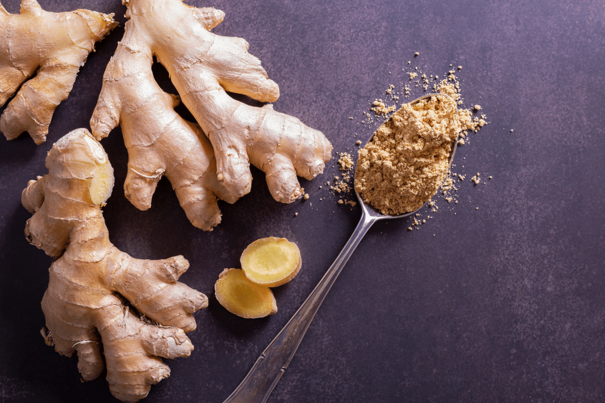 A spoonful of ginger on a dark background next to ginger roots.