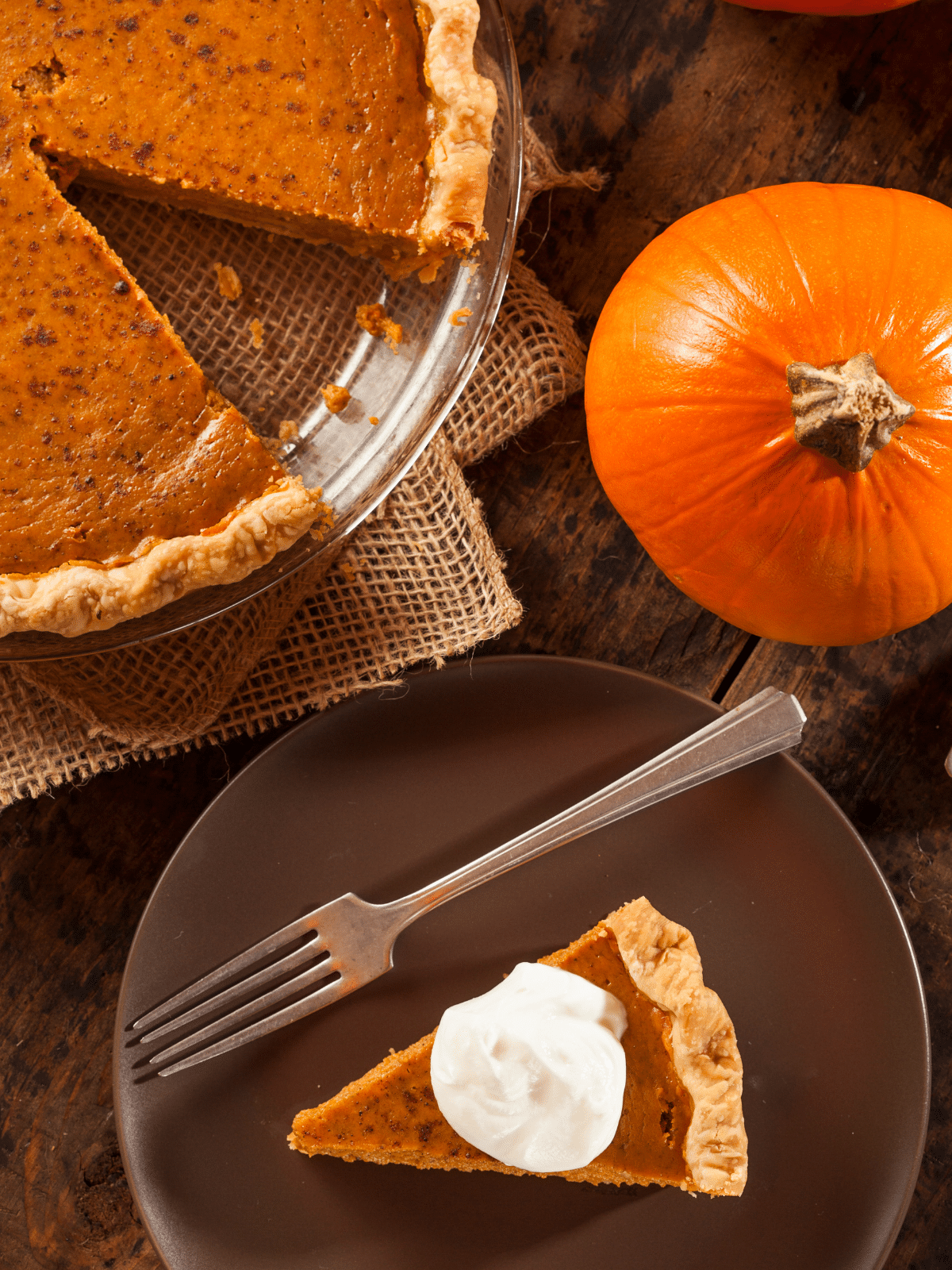 A slice of pumpkin pie on a plate with a fork. Pumpkin and sliced pumpkin pie on the side.