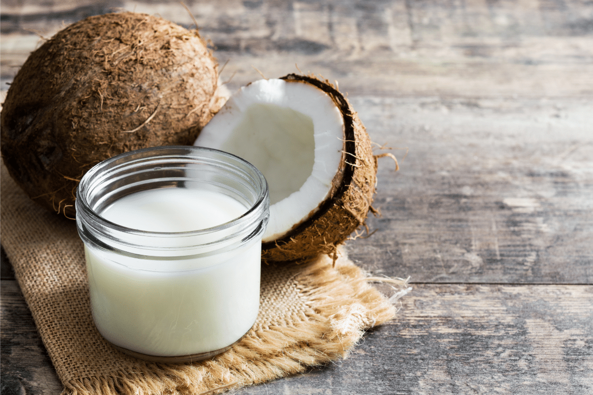 Coconut milk displayed in a jar on a wooden table with coconut on the side.