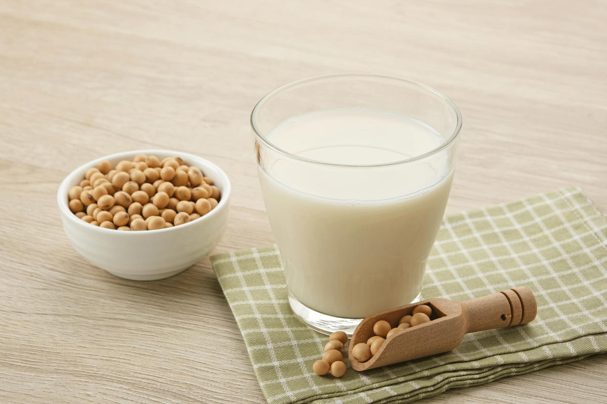 Soy milk in a glass next to soy beans in a small bowl and wooden spoon.