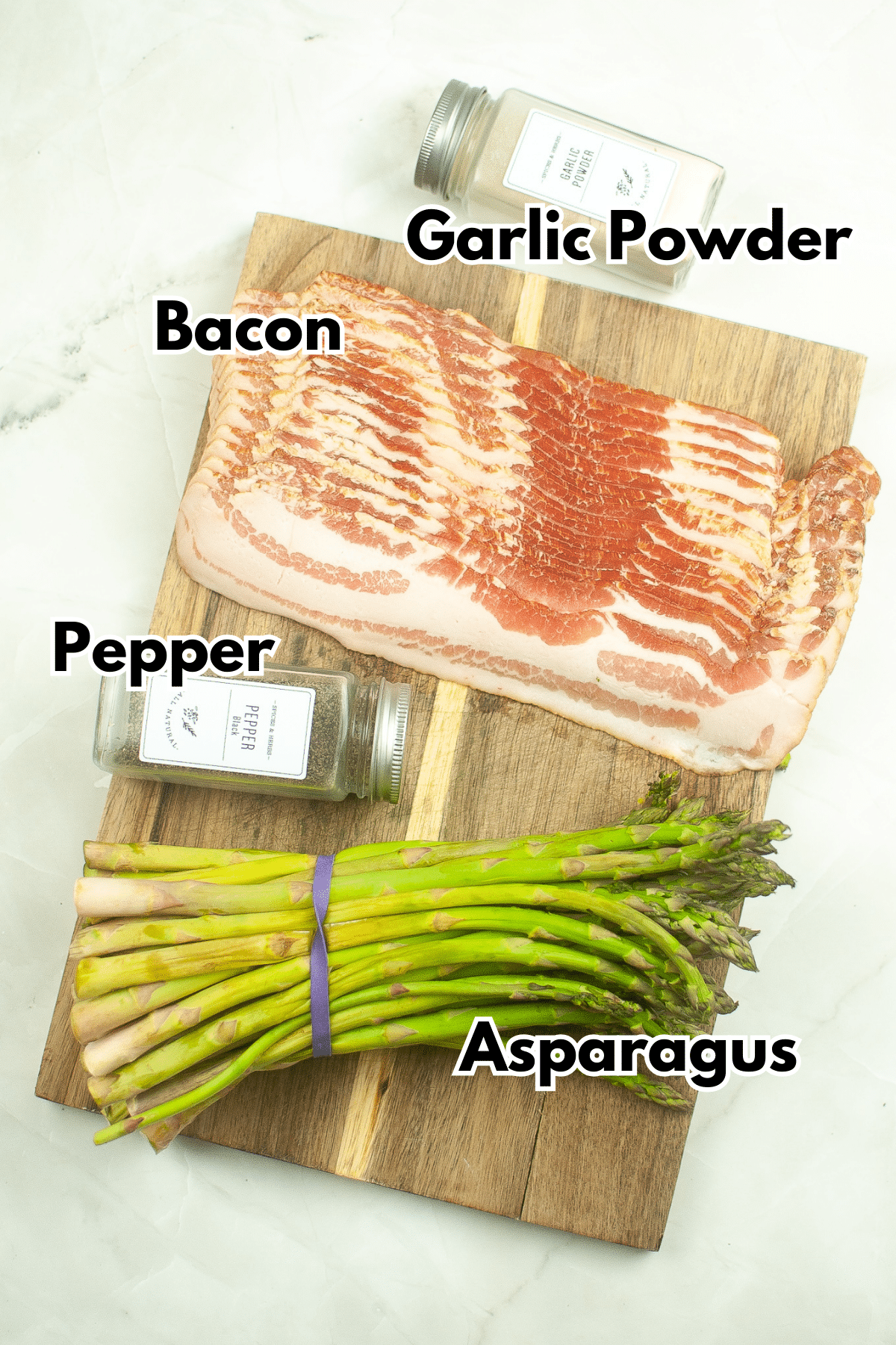 Bacon, asparagus and pepper on a cutting board next to a jar of garlic powder.
