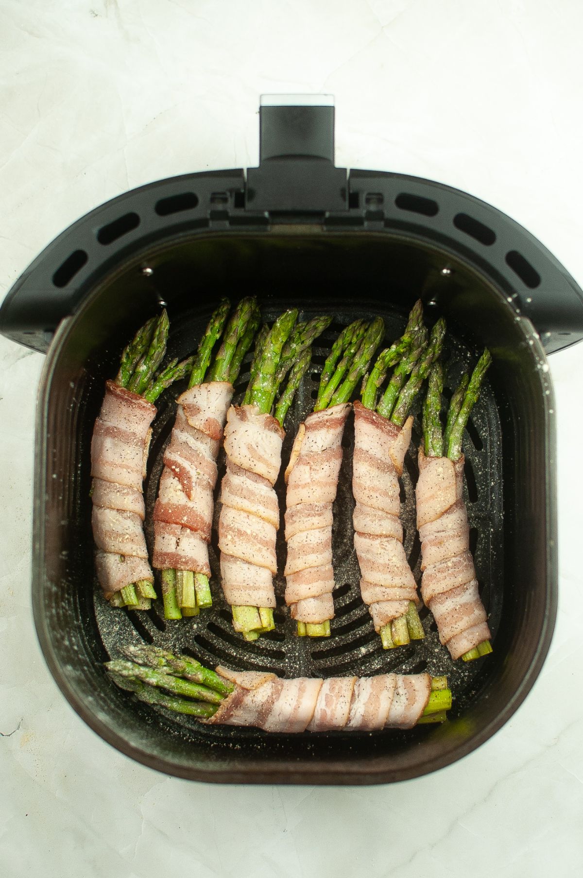 Bacon Wrapped Asparagus with seasoning inside the Air Fryer.