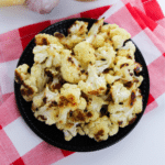 Grilled cauliflower with cheese on a red and white checkered napkin.