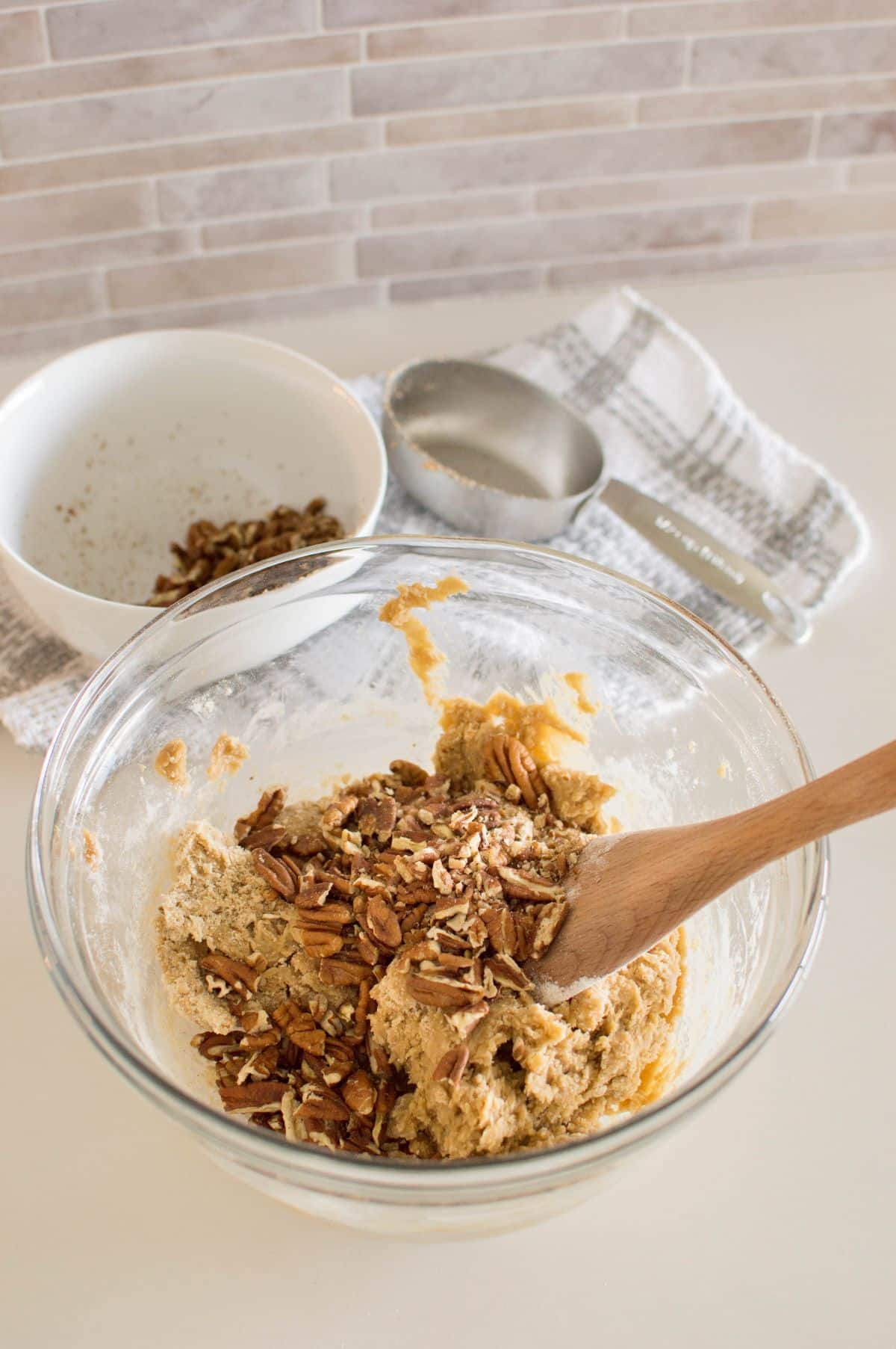 Cookie batter and pecans in a mixing bowl with wooden spoon in it.