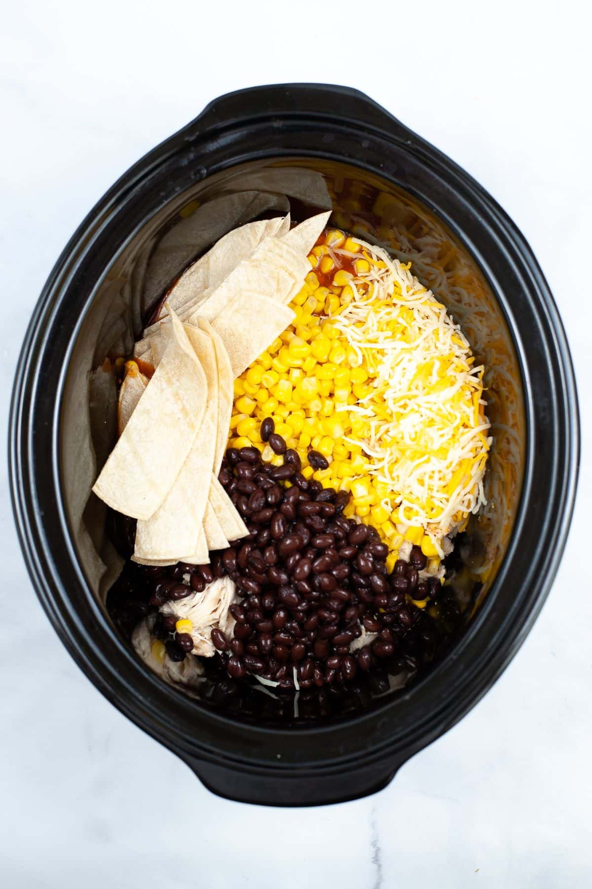 A crock pot filled with chicken enchilada casserole ingredients.