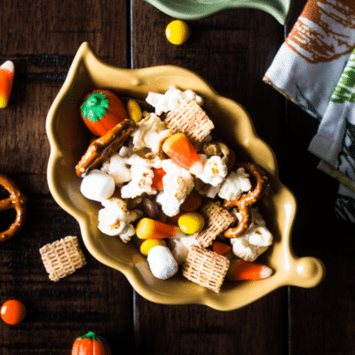 A fall party mix recipe featuring a bowl of Chex Mix with candy corn, pretzels and pretzel sticks.