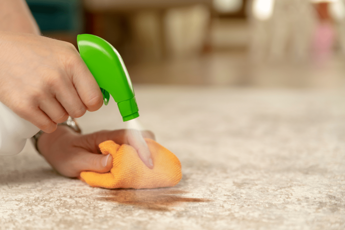 A person using a green cleaning spray to remove a coffee stain from a carpet.