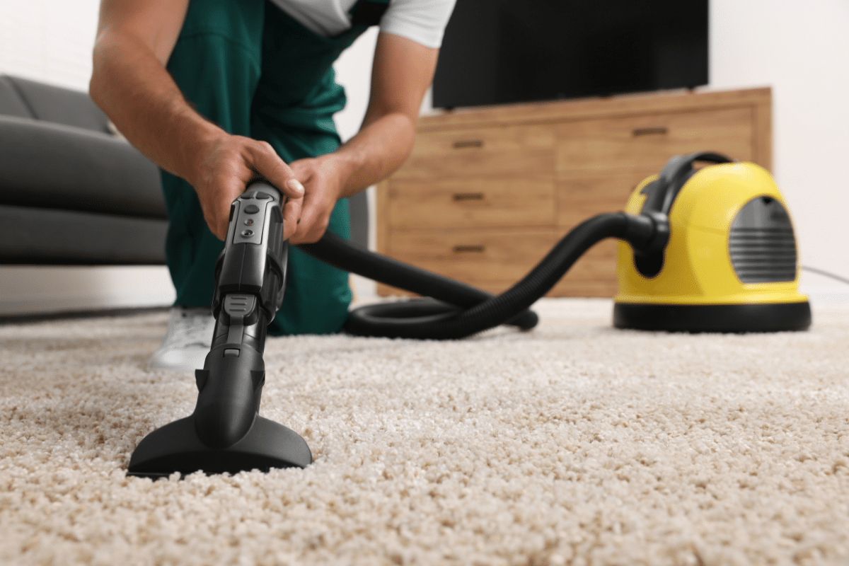 A man using a vacuum cleaner to remove red wine stains from a carpet.