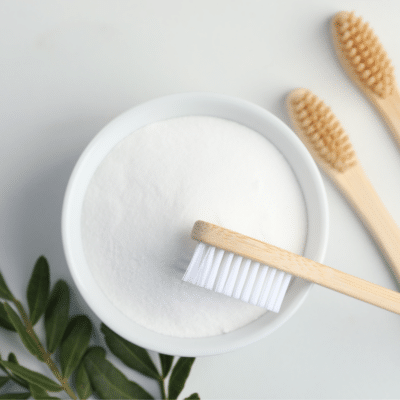 A bowl of baking soda and two toothbrushes on a white background, perfect for using baking soda for teeth.