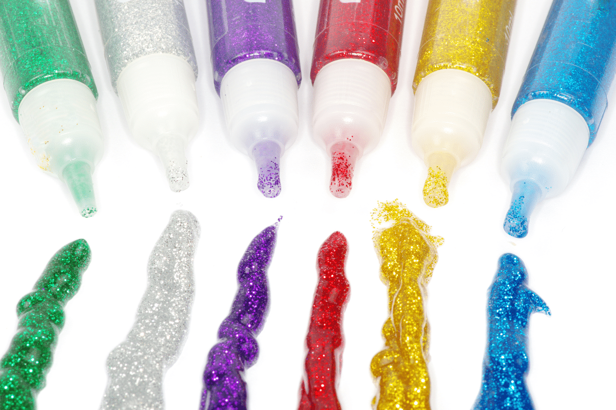 Different colored glitter glue pens on a white surface.