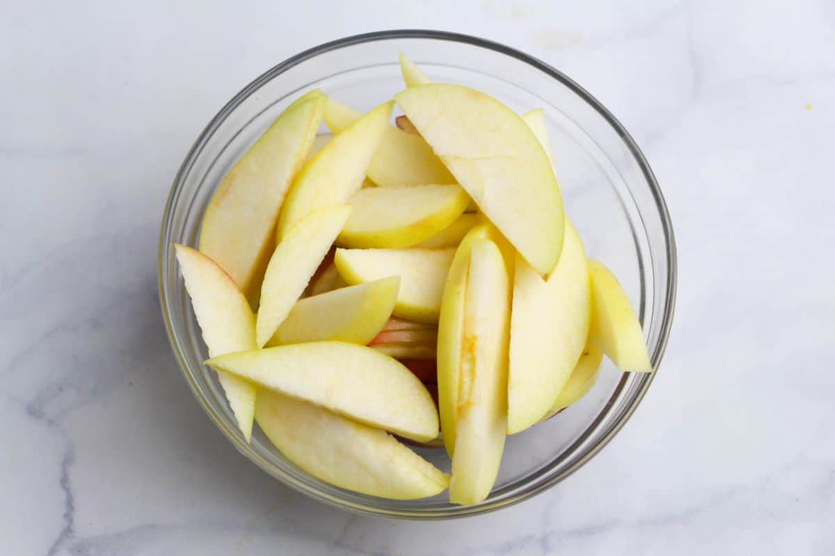 Sliced apples in a glass bowl on a white countertop.