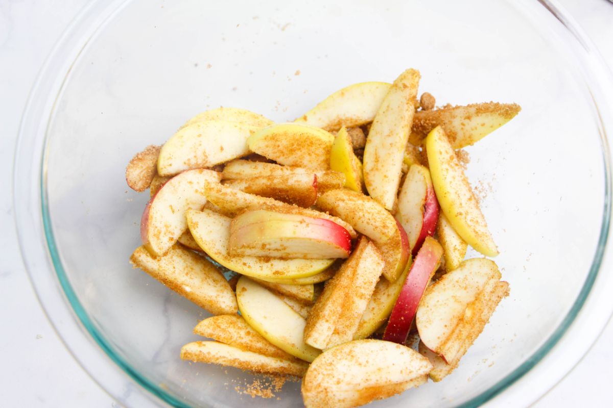 Sliced apples coated with brown sugar mixture in a glass bowl on a white countertop.