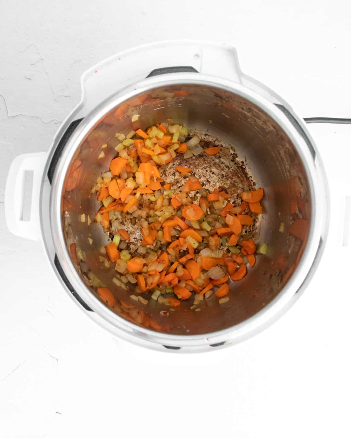 Garlic, onion, celery, and carrots are being sautéed in the Instant Pot.