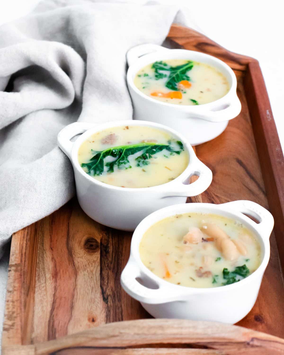 Three bowls of Kale and Sausage soup on a wooden tray.