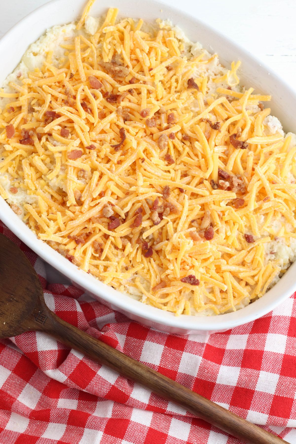 Potato mixture in the casserole dish topped with shredded cheese and bacon.