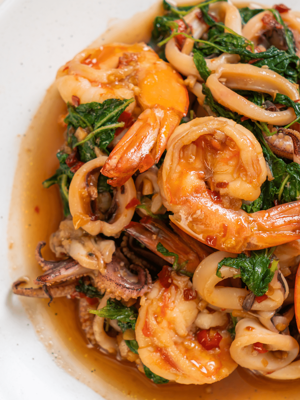Stir-fried seafood with Thai basil on a white serving plate.