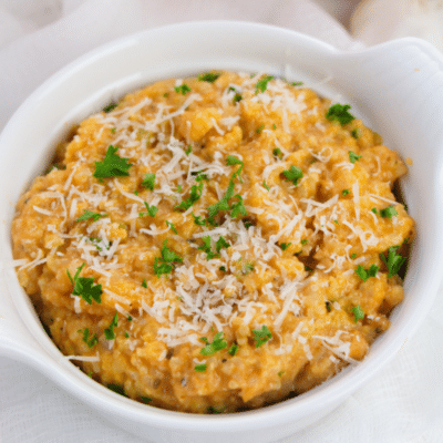 Easy pumpkin risotto served in a white bowl, garnished with parmesan cheese and parsley.