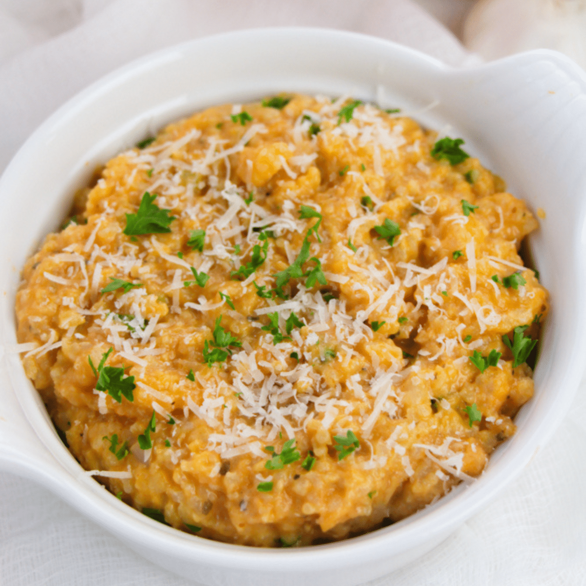 Easy pumpkin risotto in a white bowl with parmesan cheese and parsley.