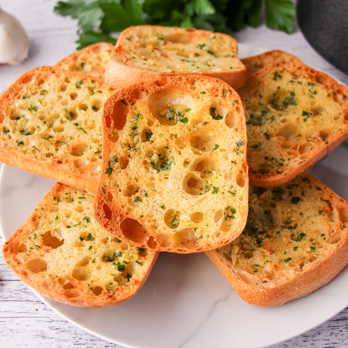 Garlic bread on a white plate with parsley.