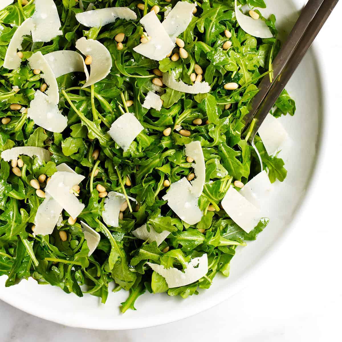 A white bowl filled with arugula and parmesan.