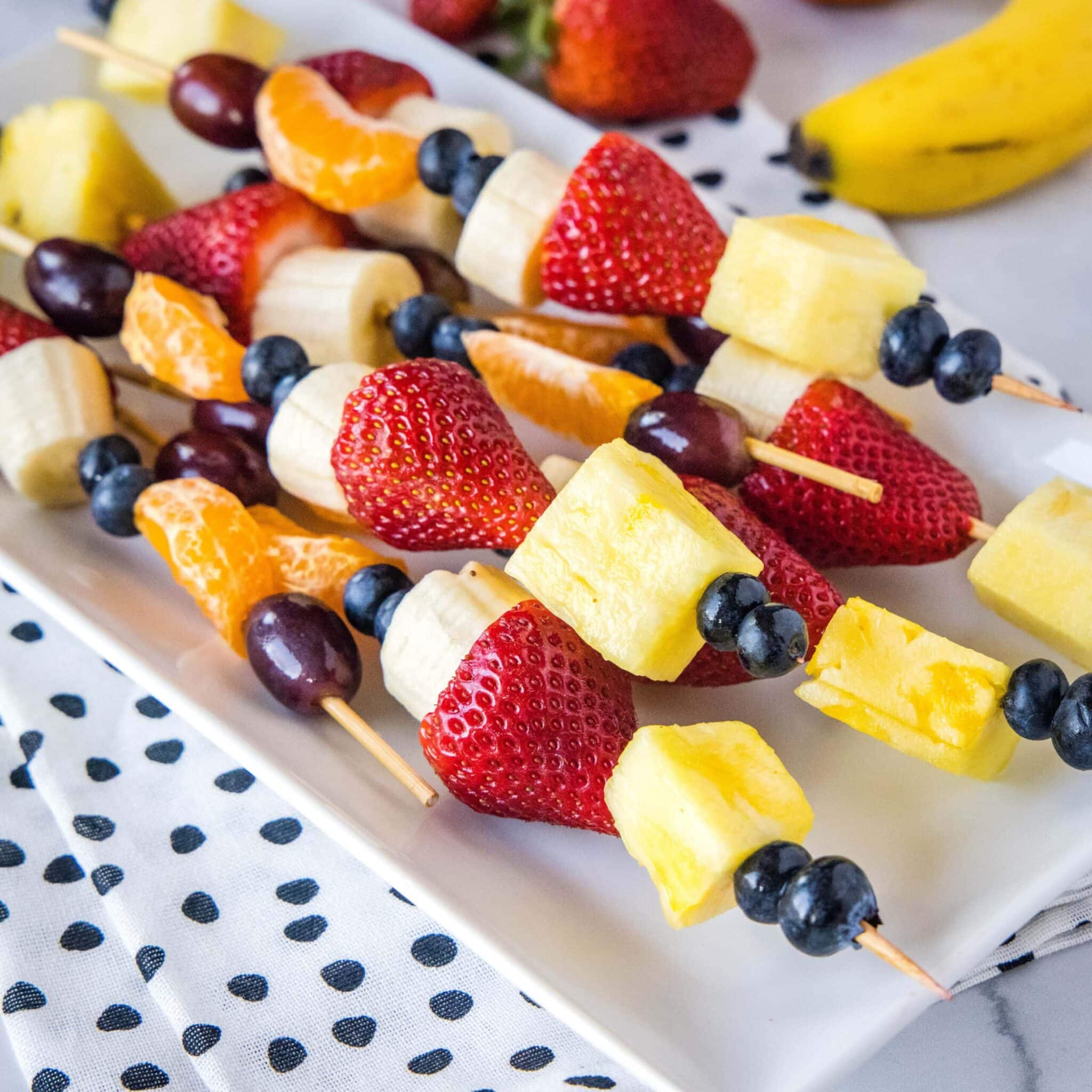 Fruit skewers on a white plate with polka dots.