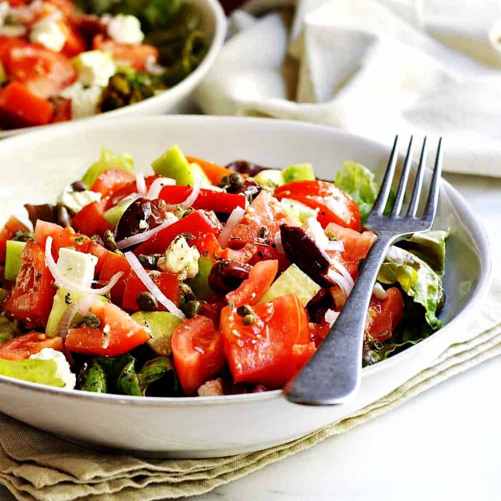 A bowl of salad with tomatoes, olives and feta cheese.