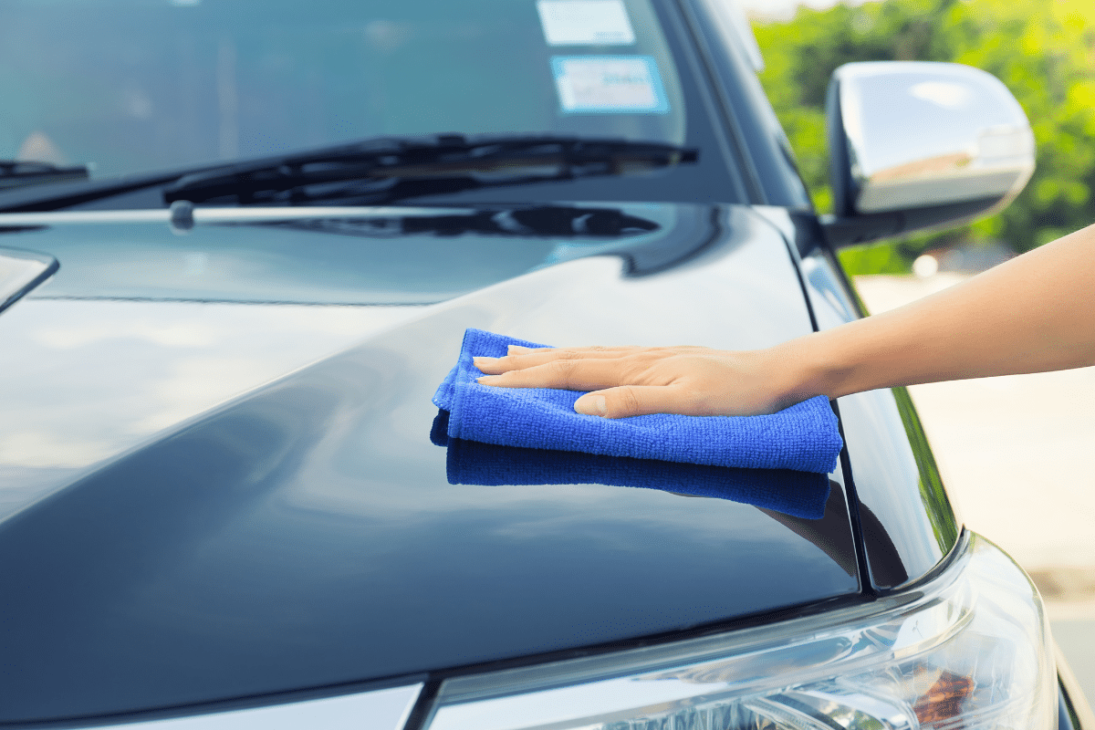 A person removing water spots from the hood of a black car with a Microfiber Cloth.