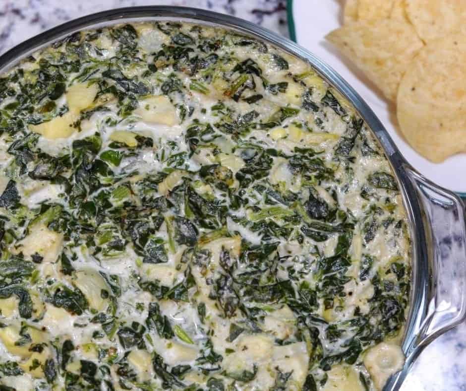 A bowl of spinach dip with chips next to it.