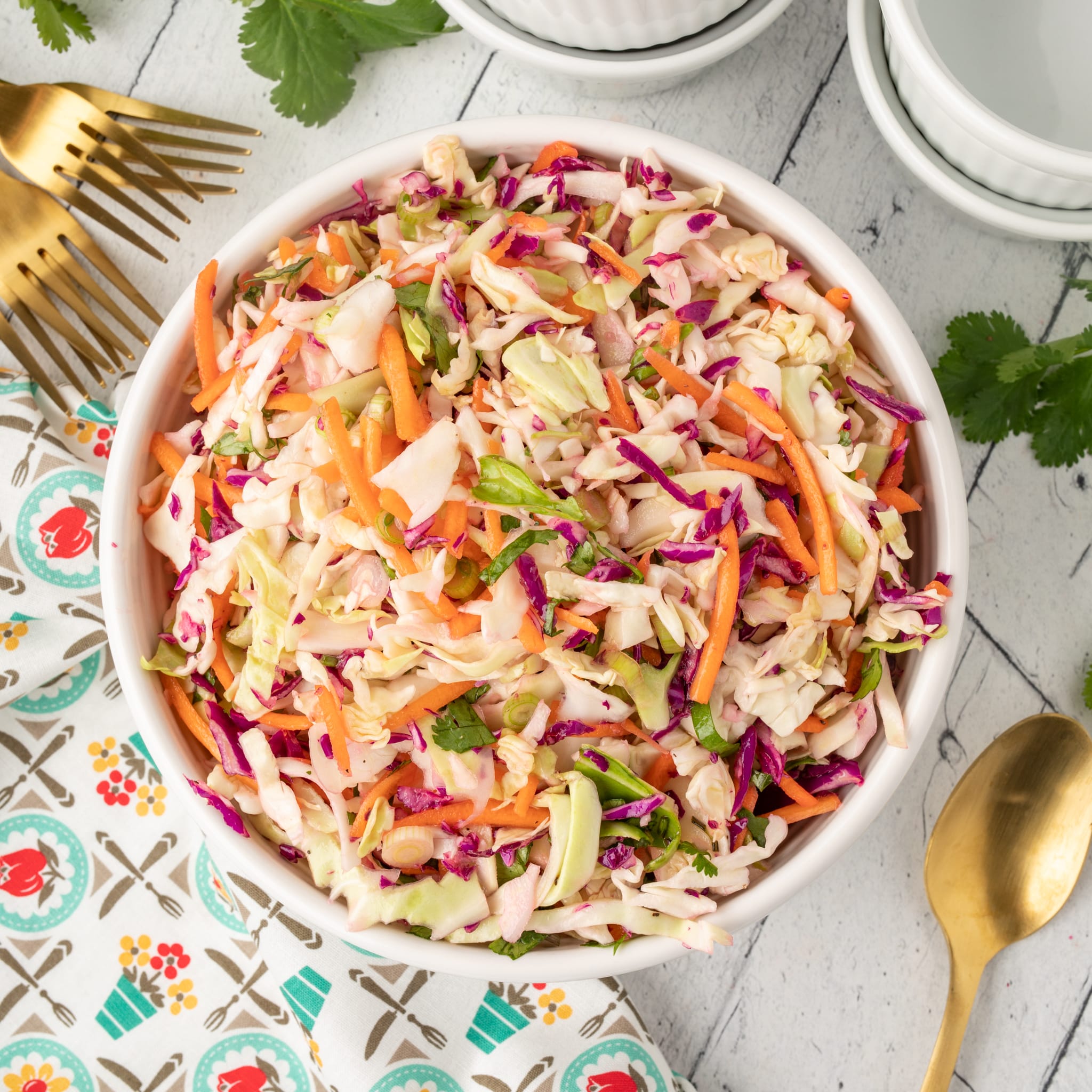 Coleslaw in a white bowl with gold spoons.
