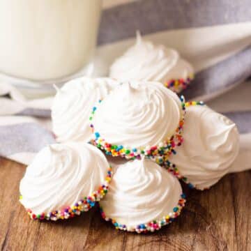 A stack of white frosted cupcakes with sprinkles and a glass of milk, perfect for a mini meringues recipe.