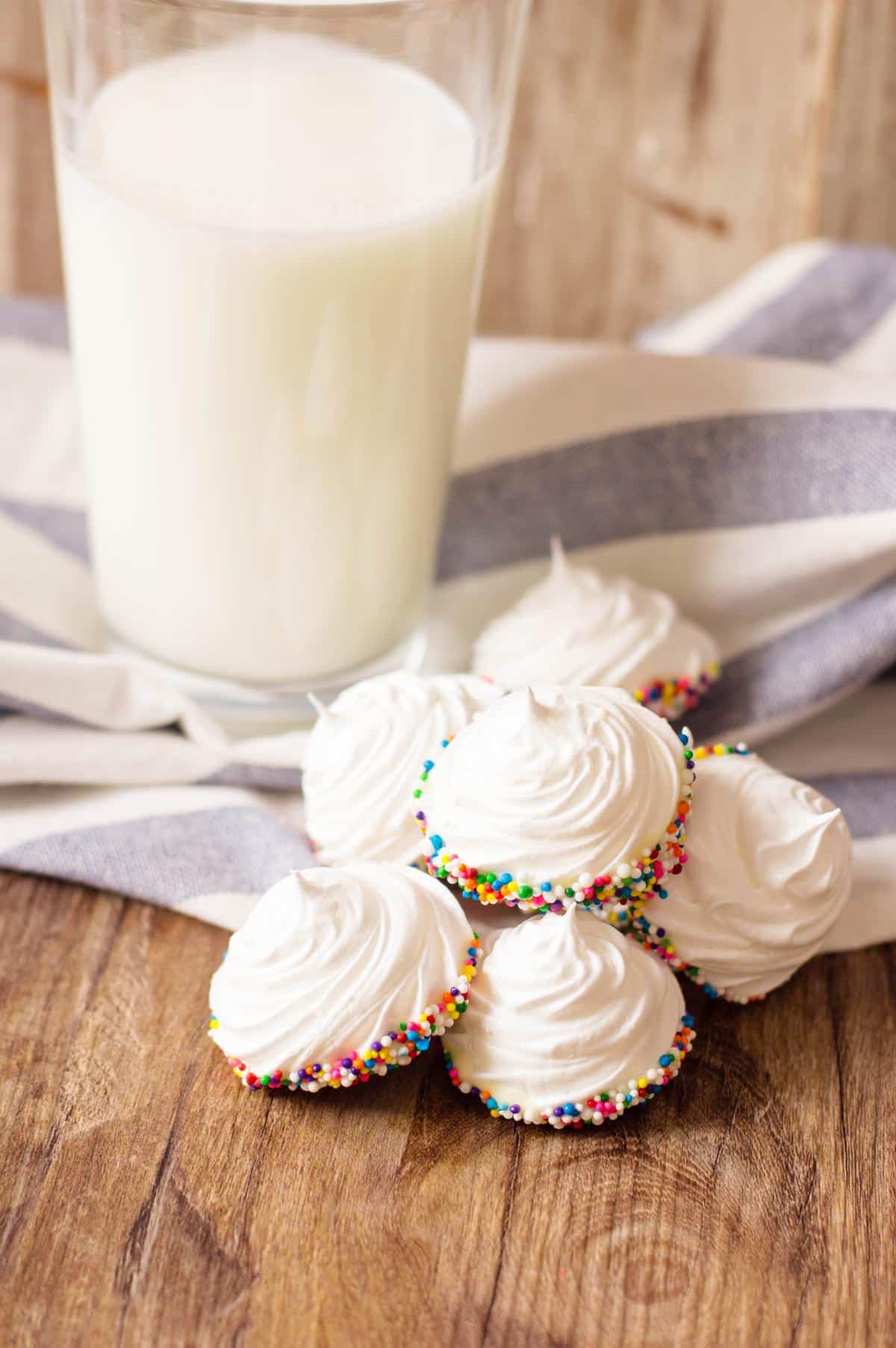Mini Meringues with sprinkles on a wooden table with a glass of milk on the side.