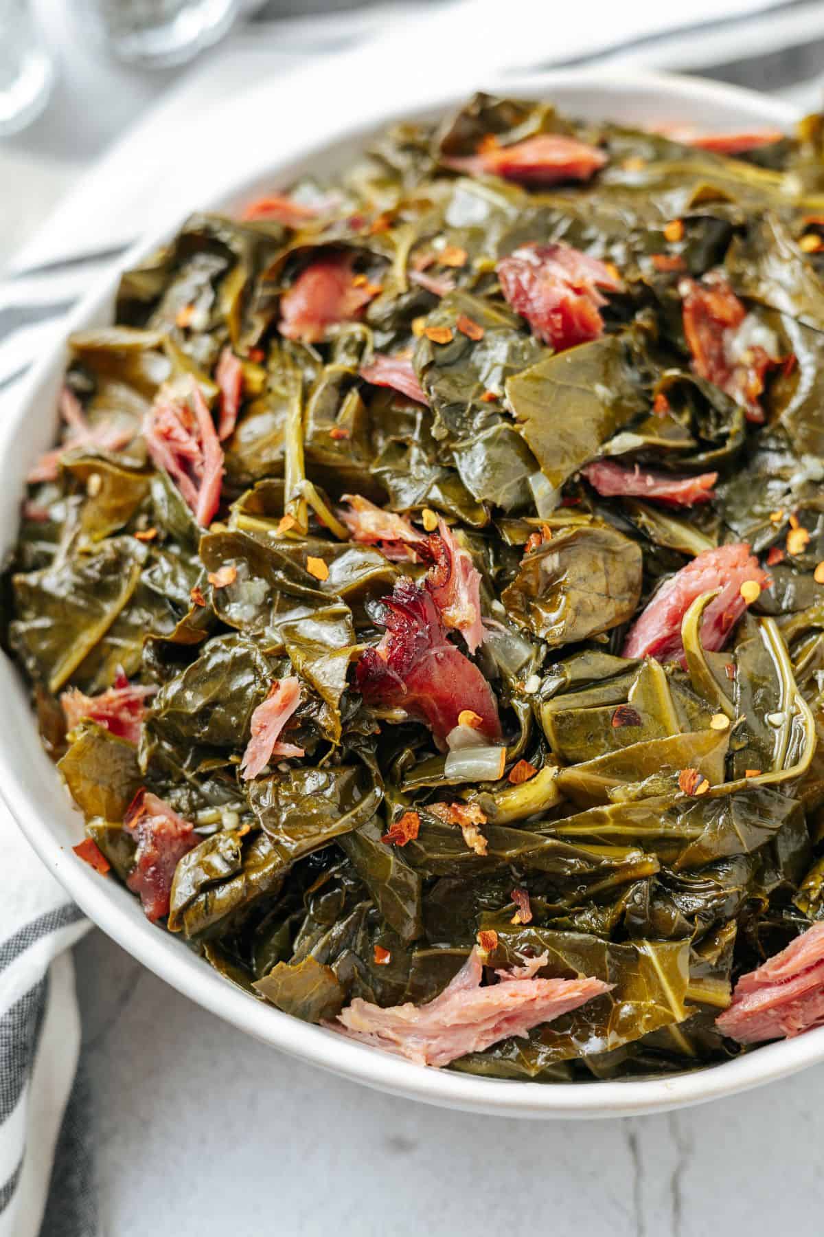 A bowl of collard greens with ham and bacon.