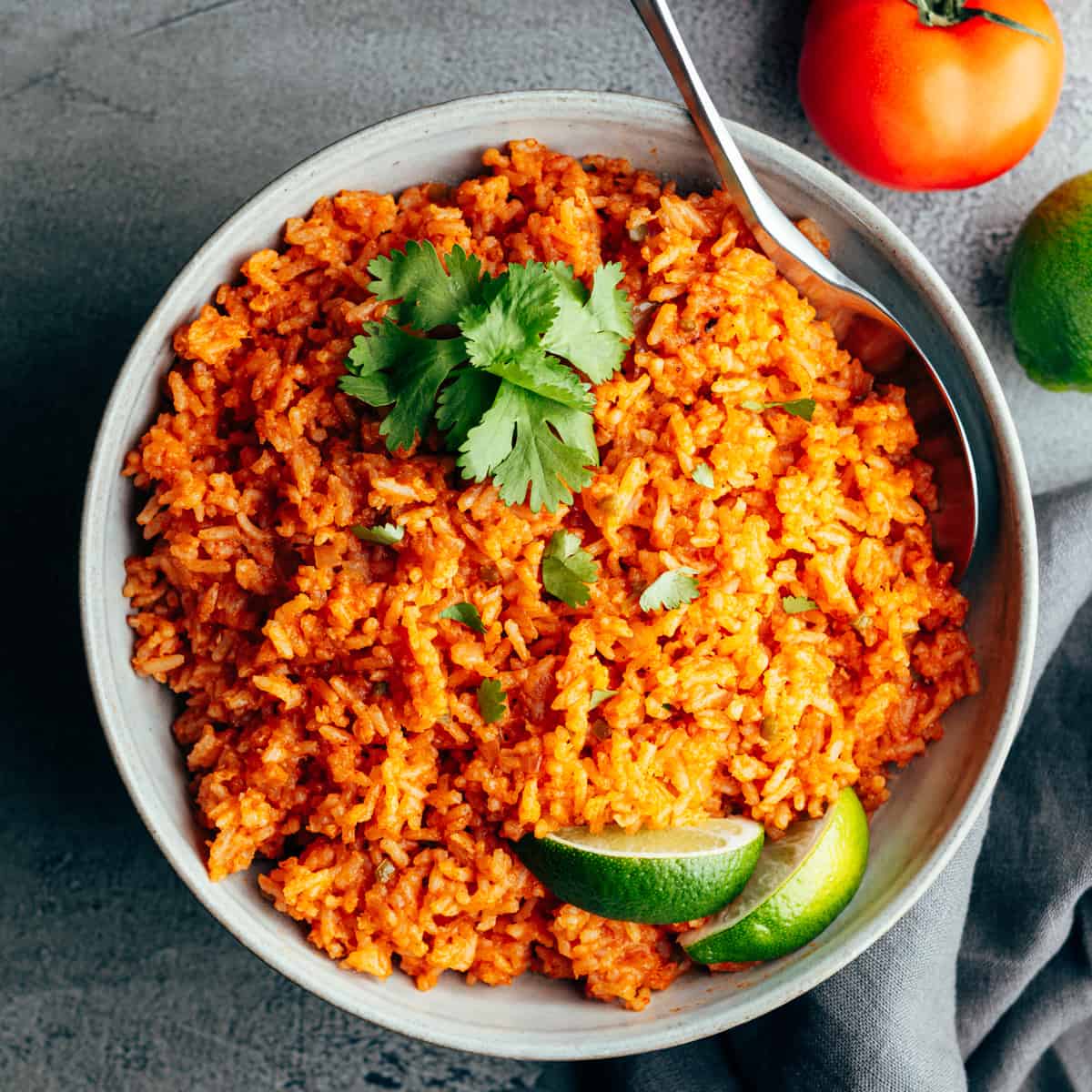 Mexican rice in a bowl with tomatoes and limes.