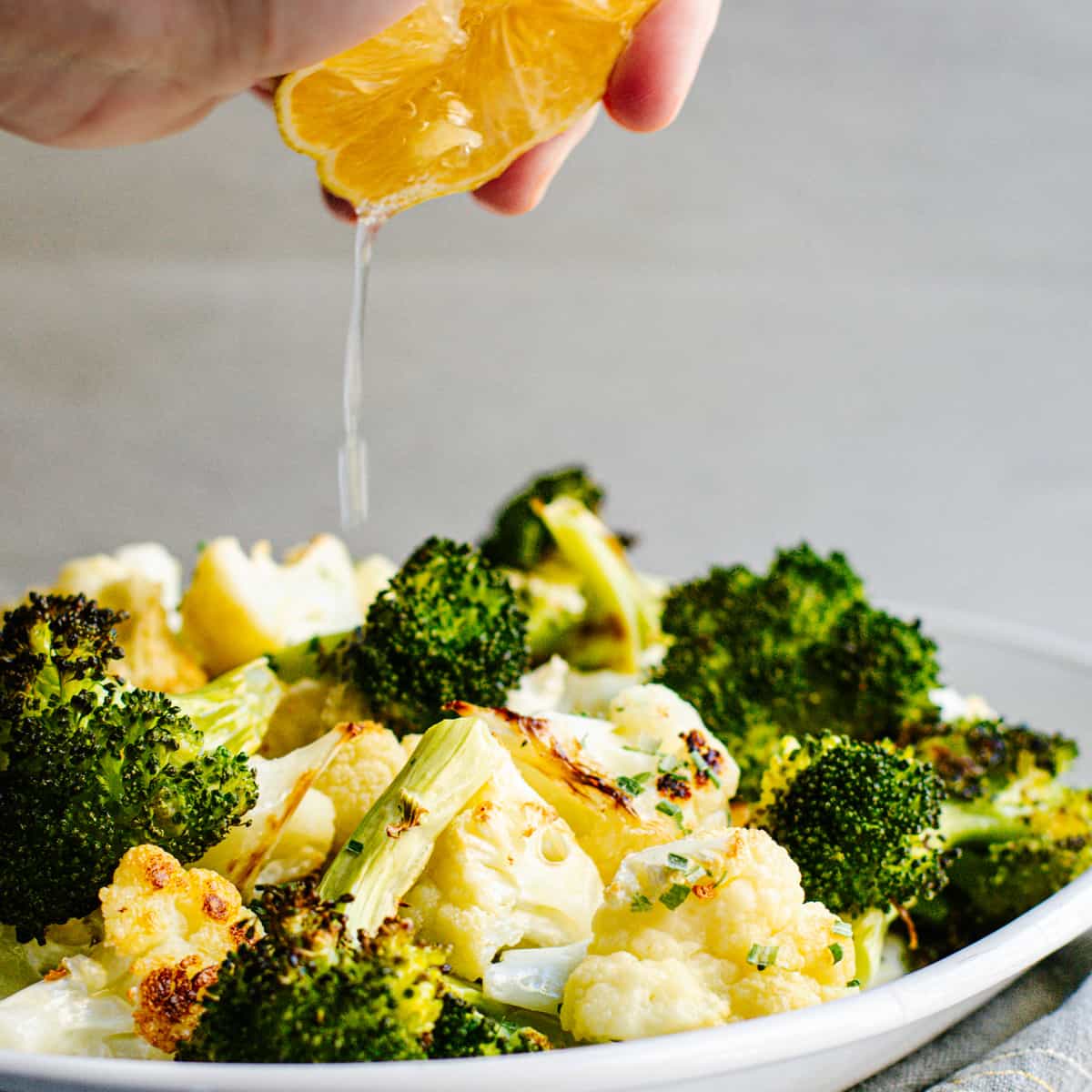 A person is squeezing an orange over a plate of broccoli and cauliflower.