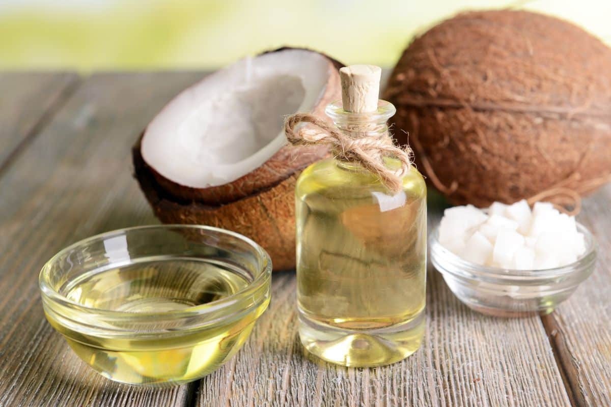 Coconut oil in a bottle and glass bowl next to coconuts.