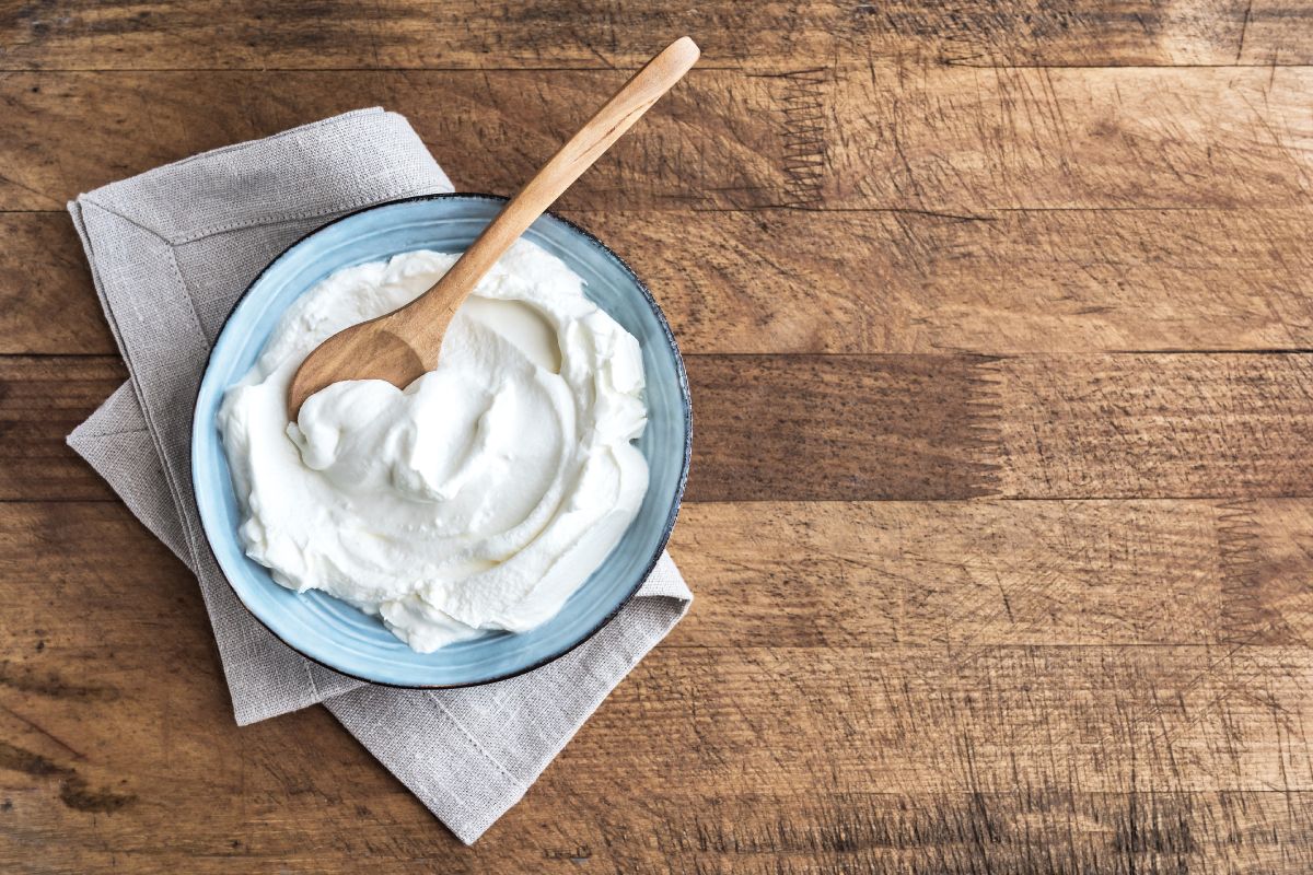 Greek Yogurt in a blue bowl on a wooden table with wooden spoon in it.