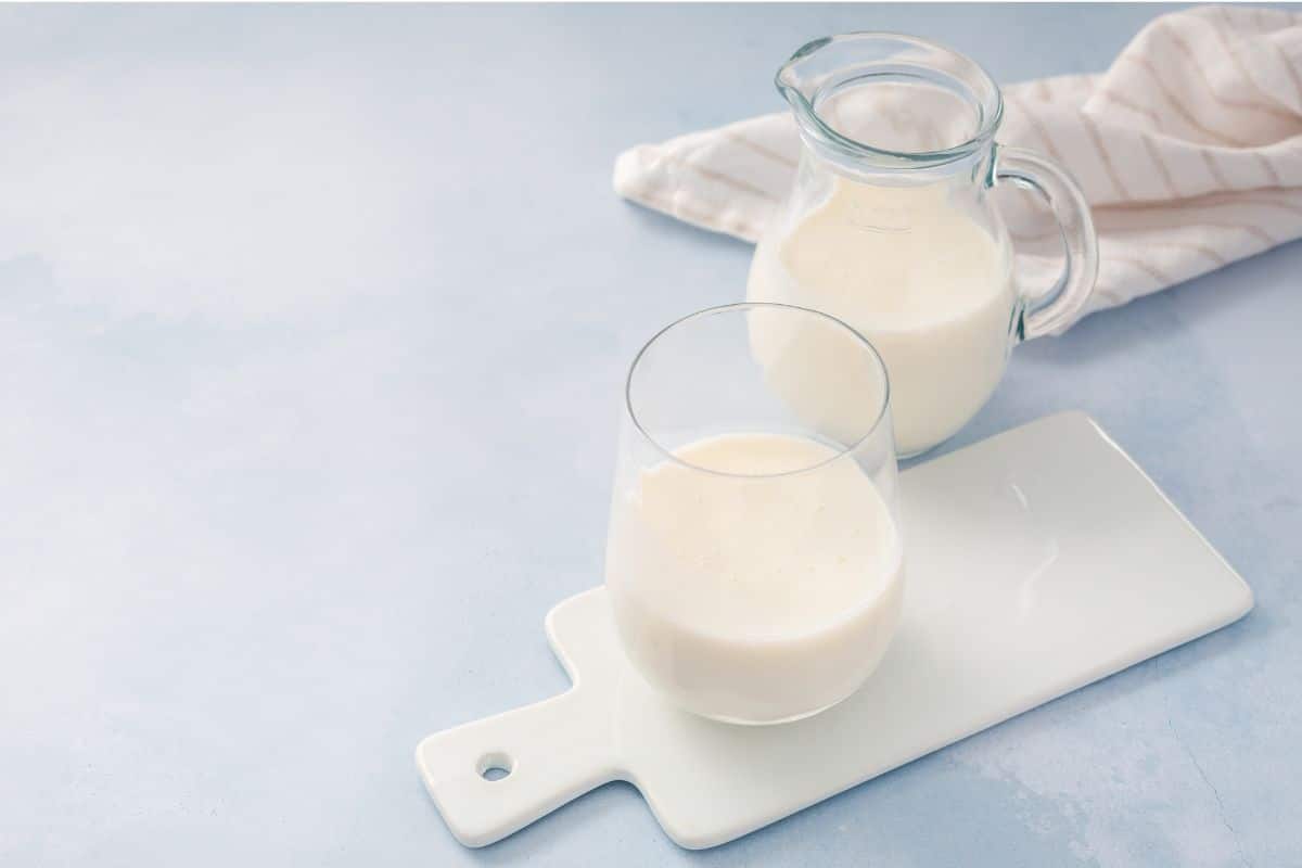 Buttermilk in a glass and glass pitcher on a white chopping board.
