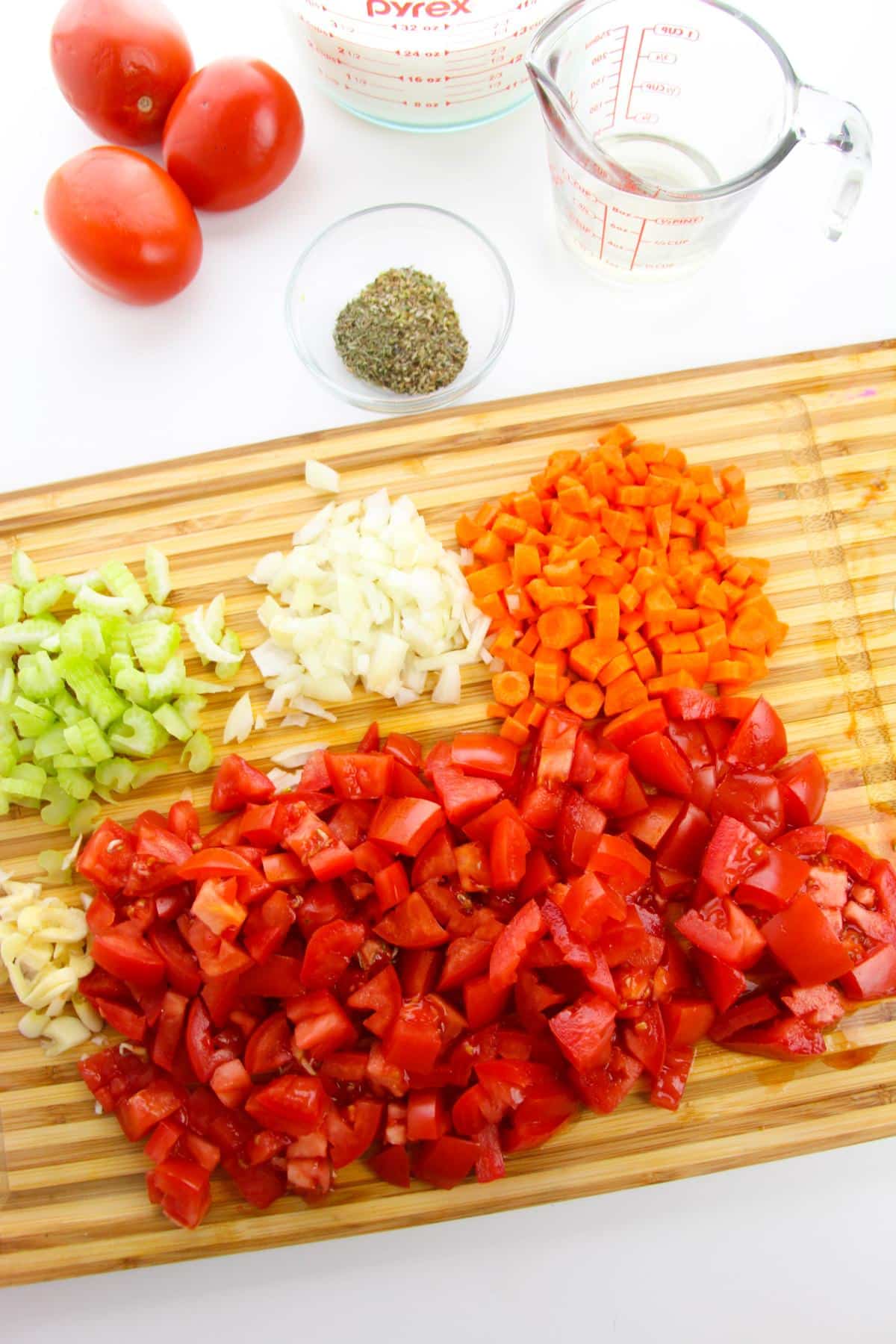 A cutting board with freshly chopped tomatoes, onions, celery, carrots and garlic.