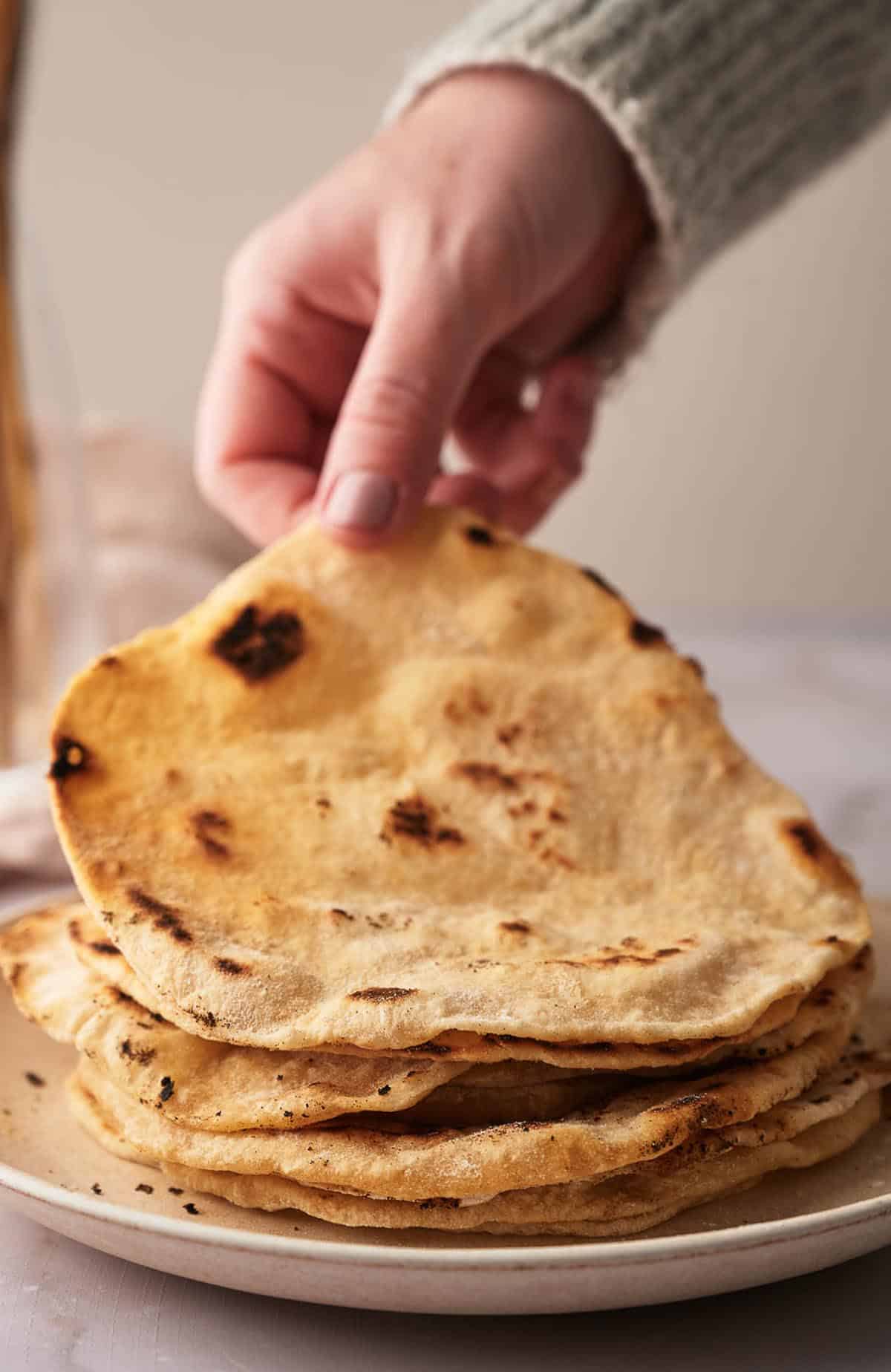 A person grabbing a stack of flatbreads on a plate.