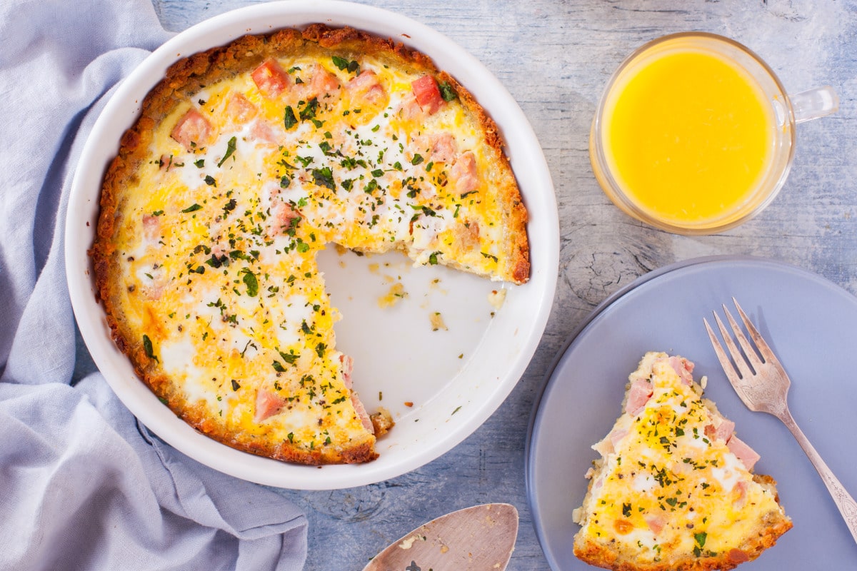 Breakfast quiche with ham and eggs on a plate with orange juice.